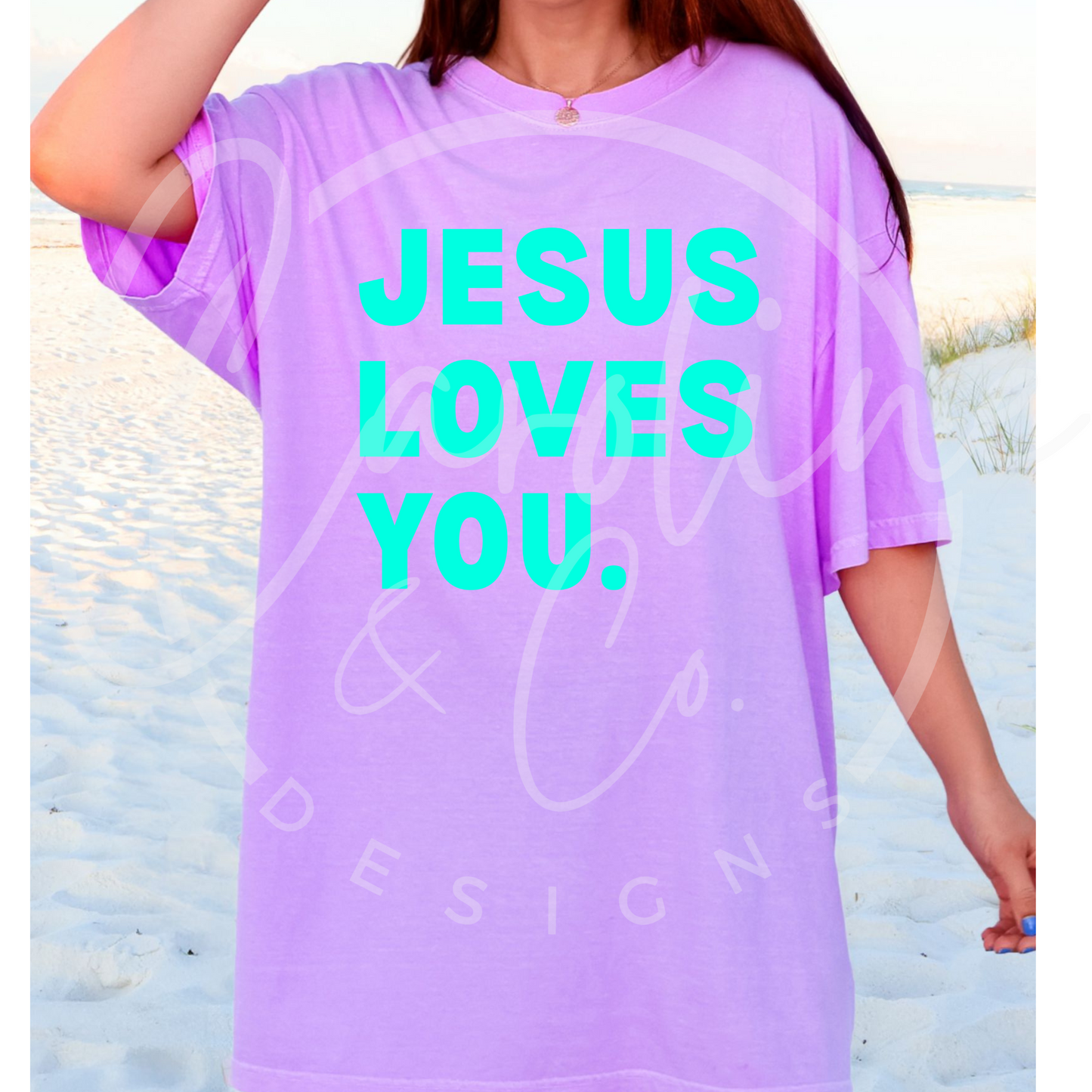 Person wearing a purple shirt with 'Jesus Loves You' text on a beach.
